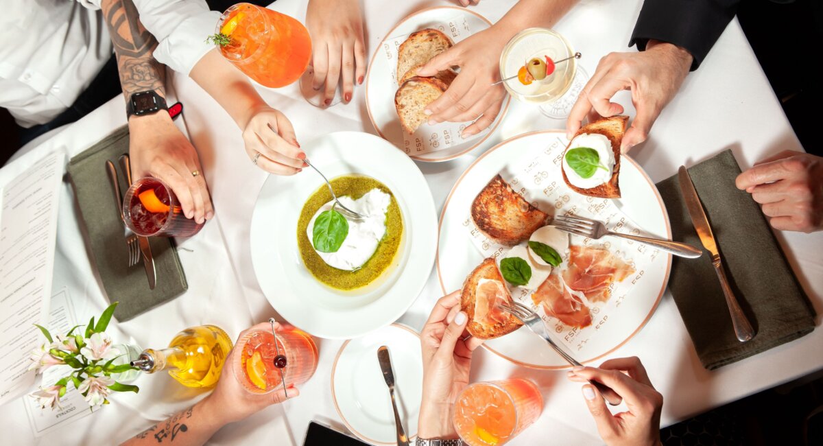Imagem com diversas mãos segurando copos com bebidas ou aperitivos da Forneria San Paolo
