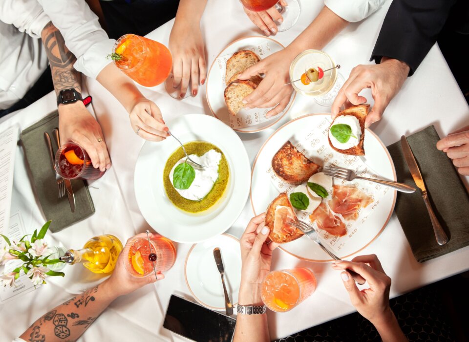 Imagem com diversas mãos segurando copos com bebidas ou aperitivos da Forneria San Paolo