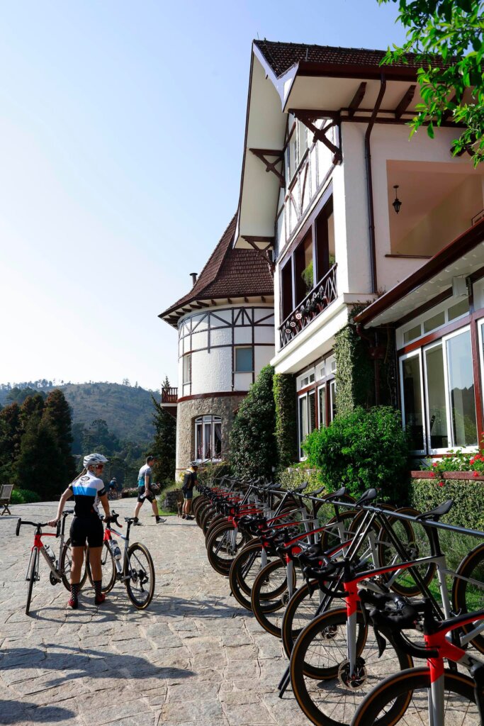 Ciclista com sua bicicleta na entrada do Hotel Vila Inglesa, destacando a estrutura de recepção para os atletas.